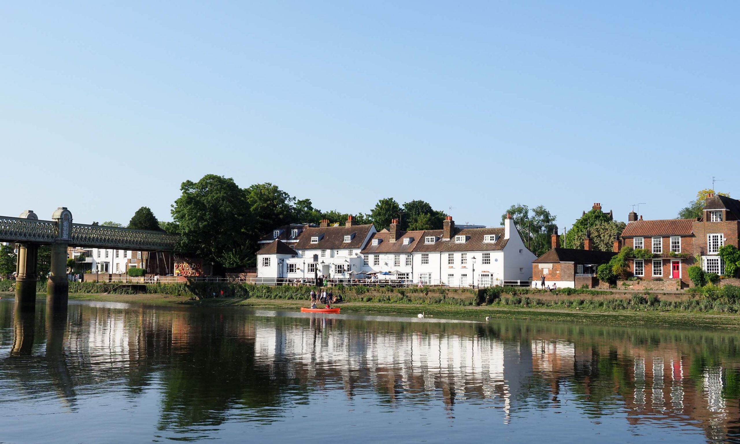 Tranquil evening scene on the River Thames with a red canoe passing a whitewashed pub