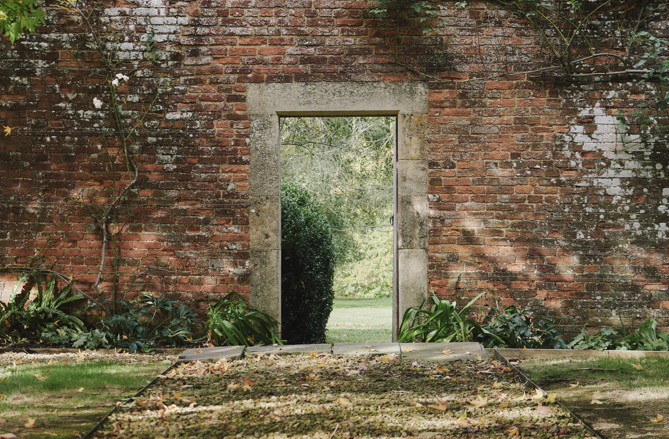 Garden doorway through weathered brick wall revealing verdant grounds at Havenwood exclusive countryside rental in The Cotswolds.