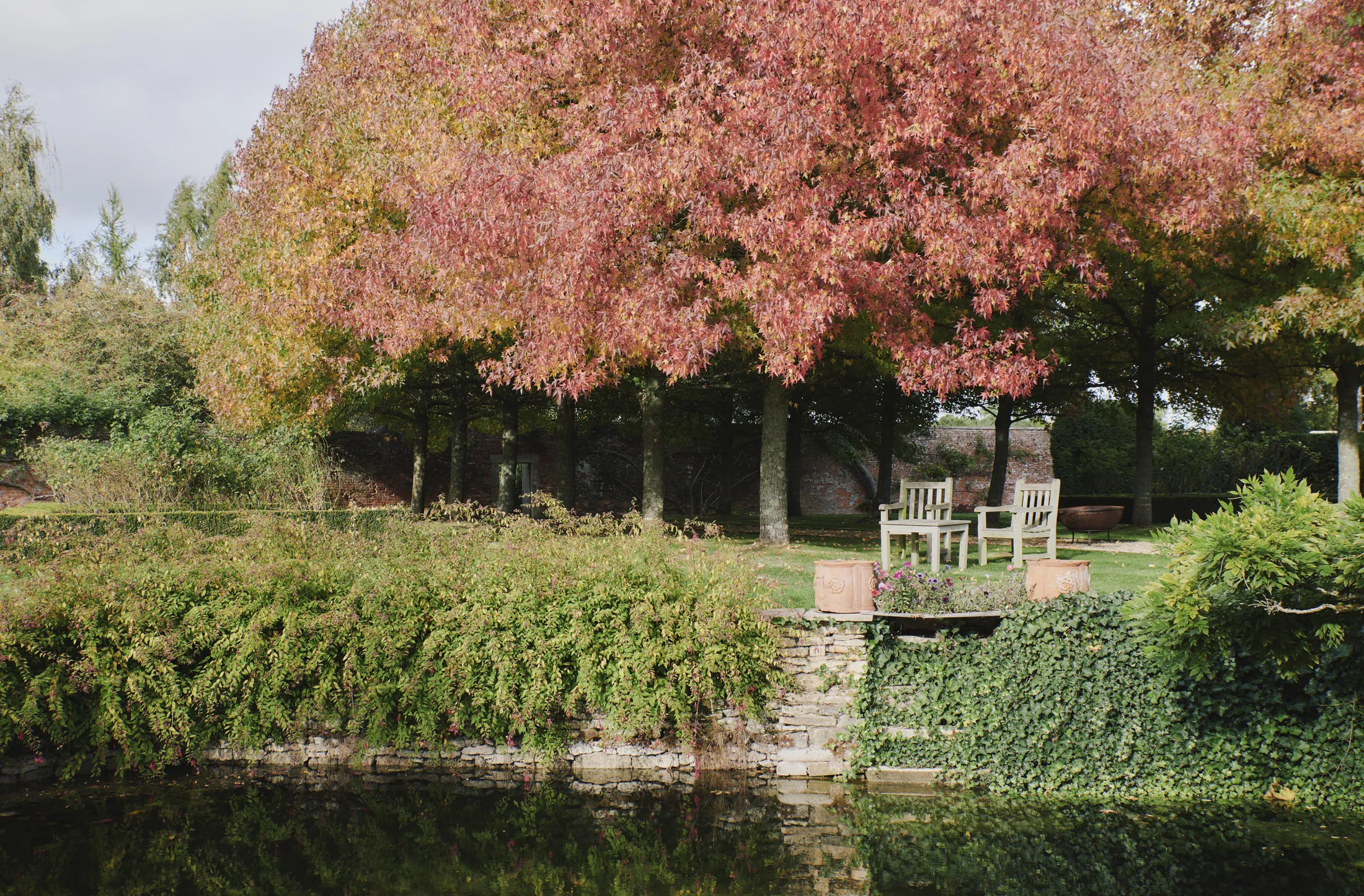 Autumn woodland seating beside reflective pond at Havenwood exclusive short stay retreat in The Cotswolds.