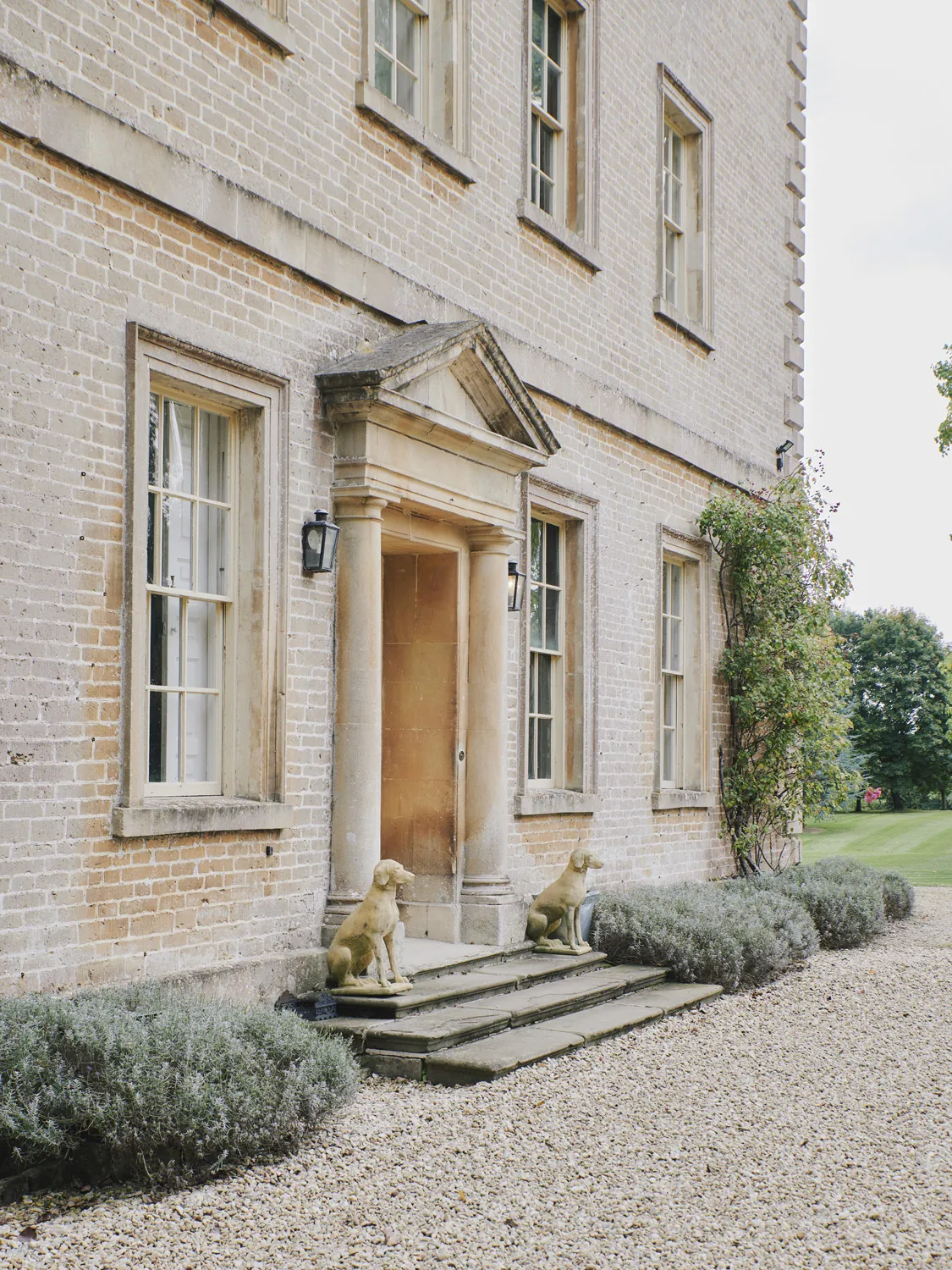 Grand entrance with stone steps flanked by decorative hounds and lavender borders at Havenwood, a luxury short term rental in The Cotswolds.