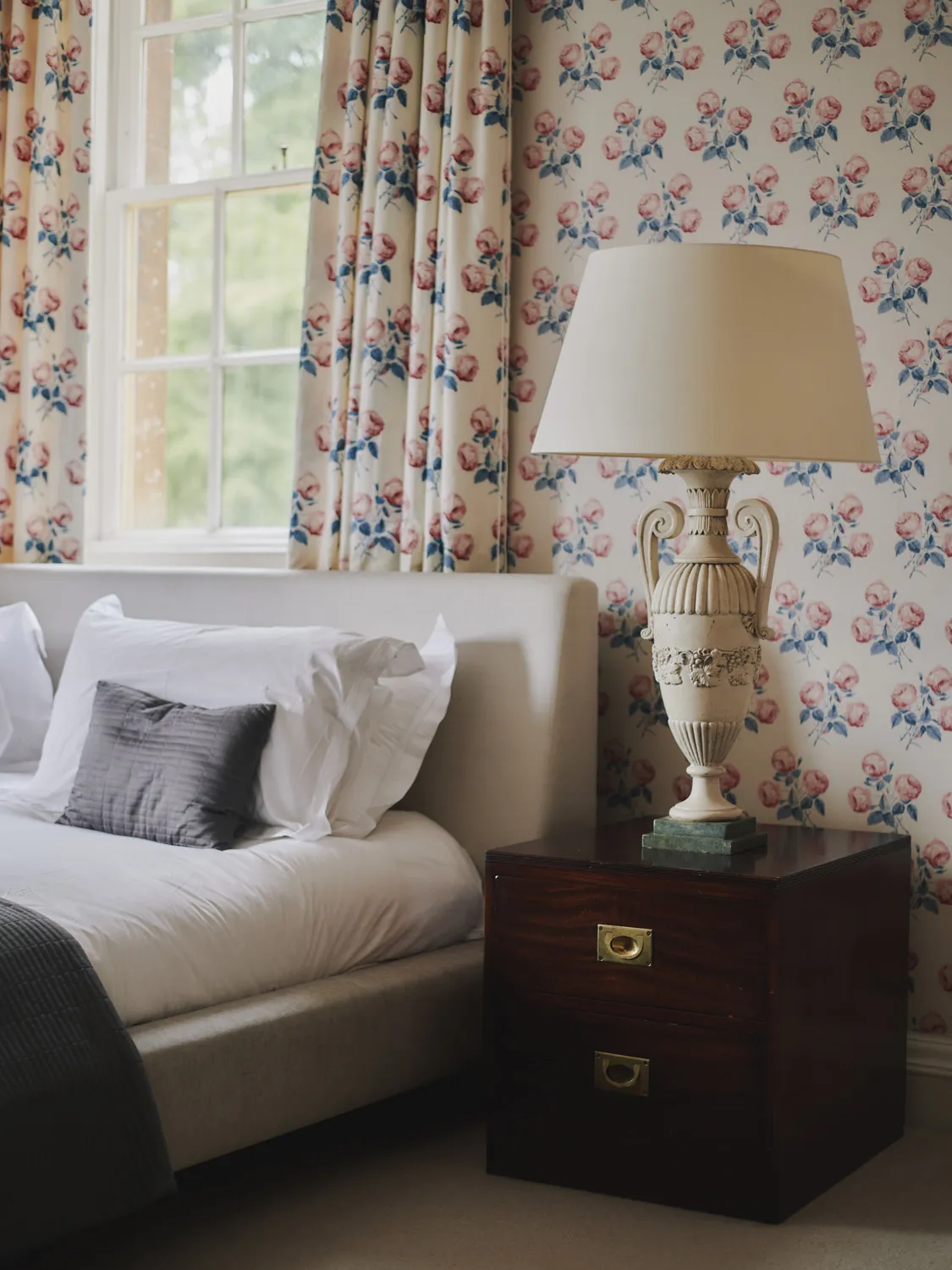 Bedroom corner with rose-patterned wallpaper and turned-wood lamp at Havenwood luxury short term property in The Cotswolds.