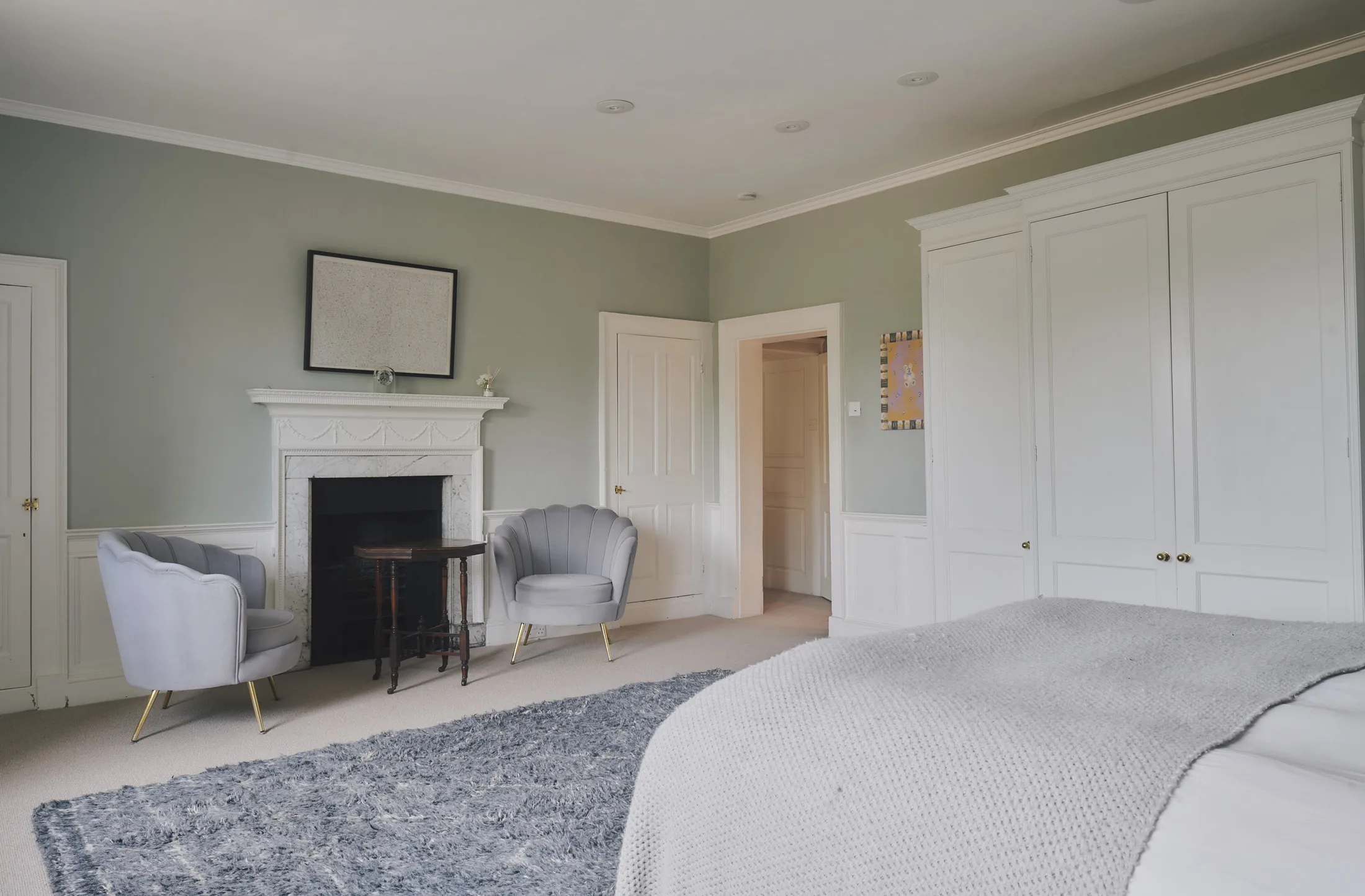 Sophisticated bedroom with sage walls, fireplace, and fitted wardrobes at Havenwood luxury short term property in The Cotswolds.