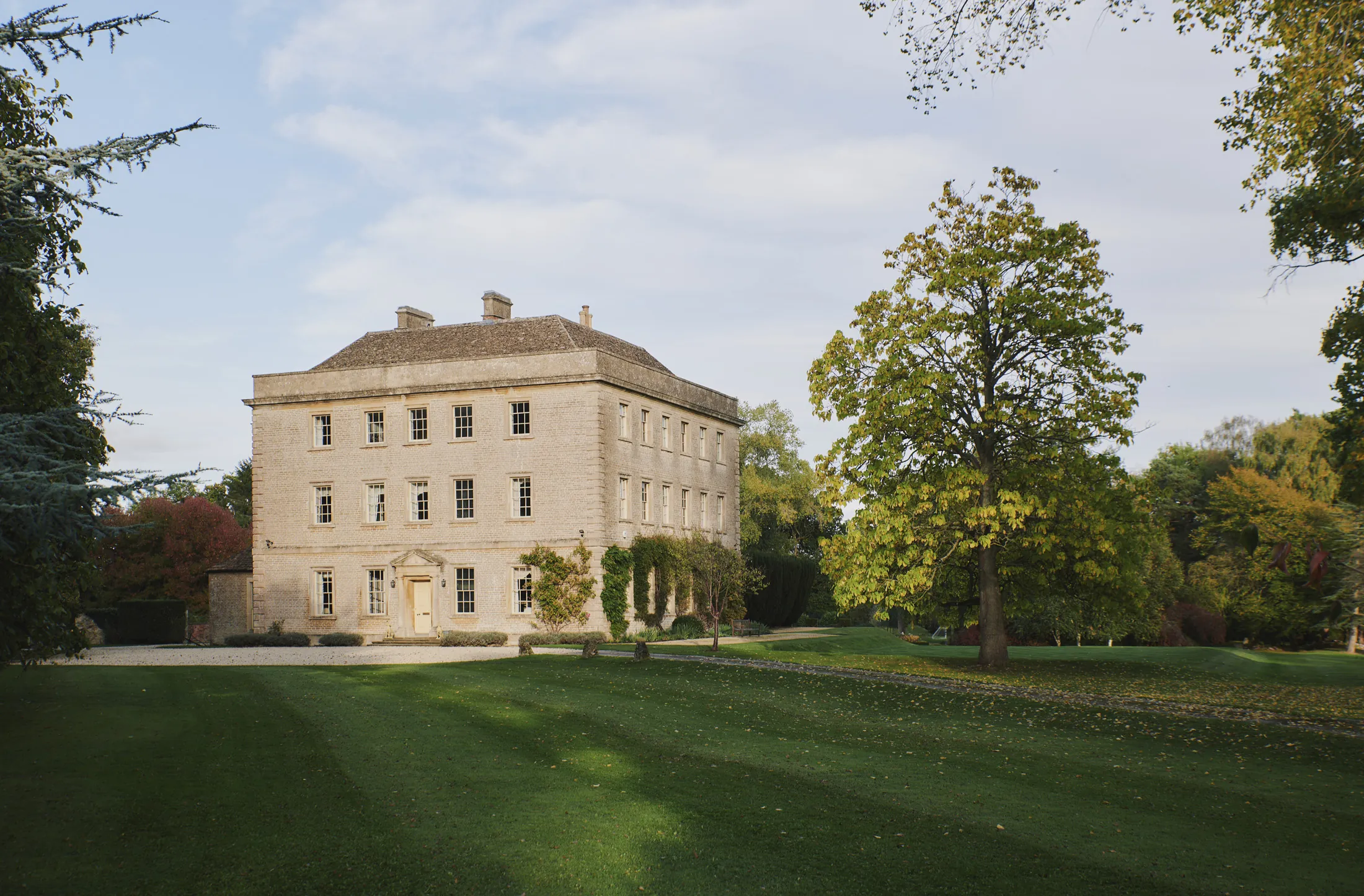 Symmetrical stone facade set within sweeping lawns and woodland at Havenwood luxury short term getaway in The Cotswolds.