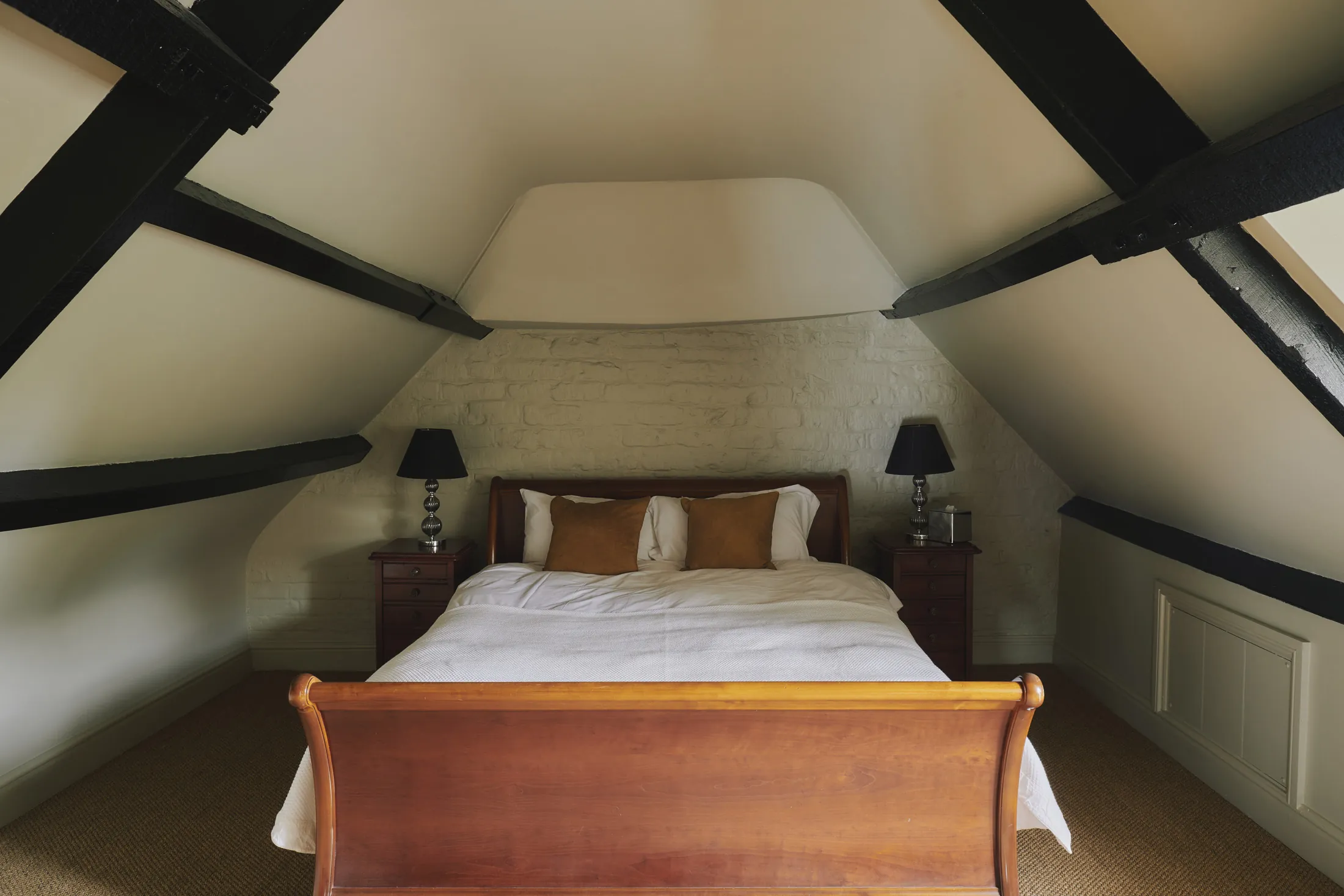 Eaves bedroom with wooden bed frame and vaulted beamed ceiling at Havenwood exclusive countryside rental in The Cotswolds.