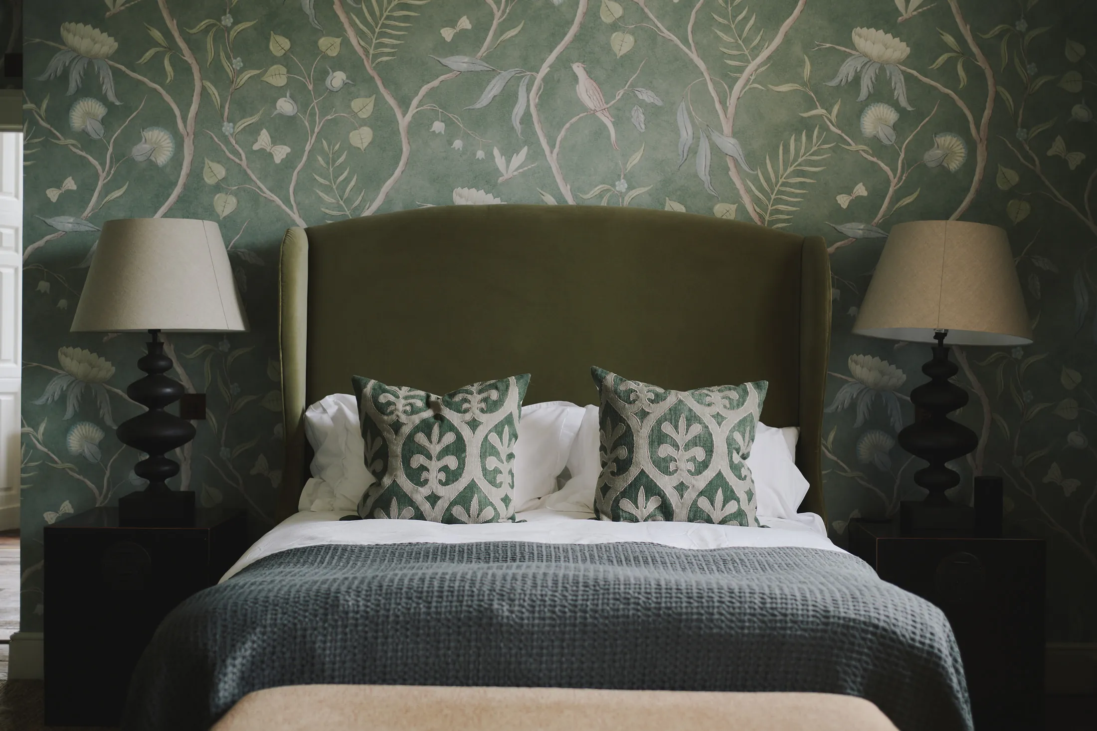Tranquil bedroom with sage green upholstered headboard and botanical wallpaper at Havenwood exclusive property in The Cotswolds.