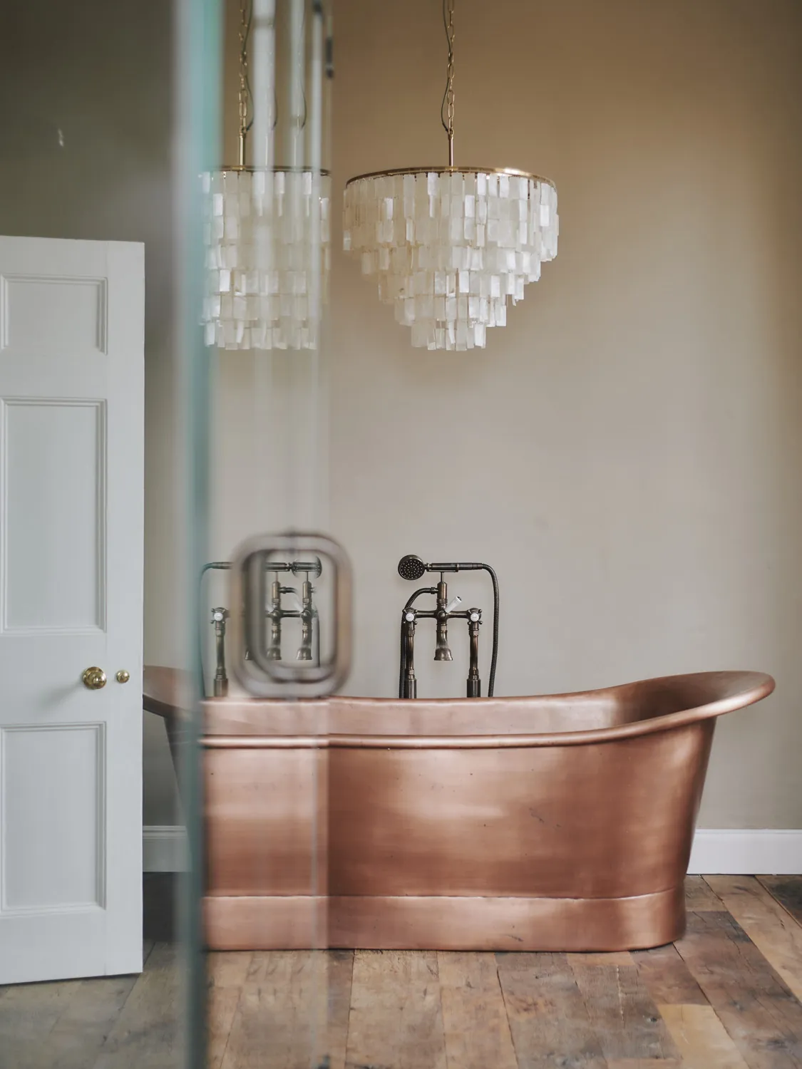 Copper roll-top bath beneath statement chandelier on timber floors at Havenwood, a Domus Stay luxury property for relaxing escapes.