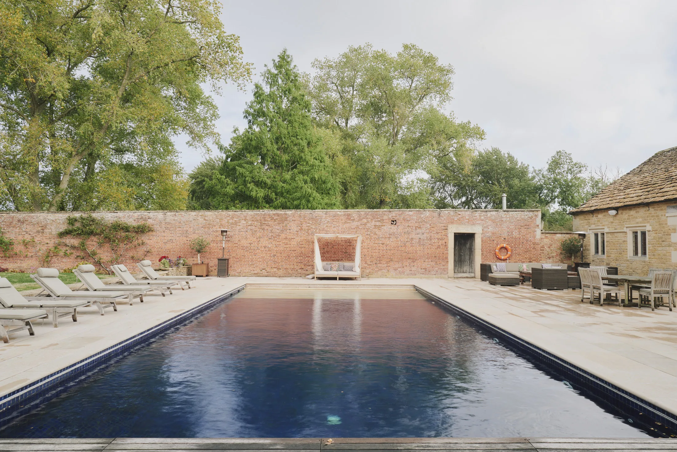 Outdoor swimming pool with loungers and dining terrace surrounded by mature gardens at Havenwood, a Domus Stay luxury getaway.