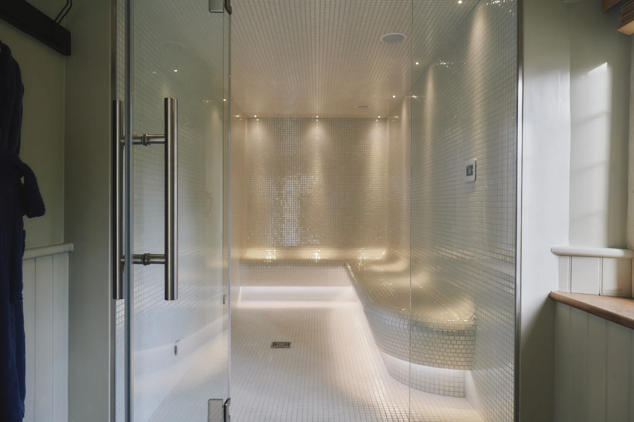 Steam room with curved tiled benches and ambient lighting at Havenwood exclusive countryside retreat in The Cotswolds.