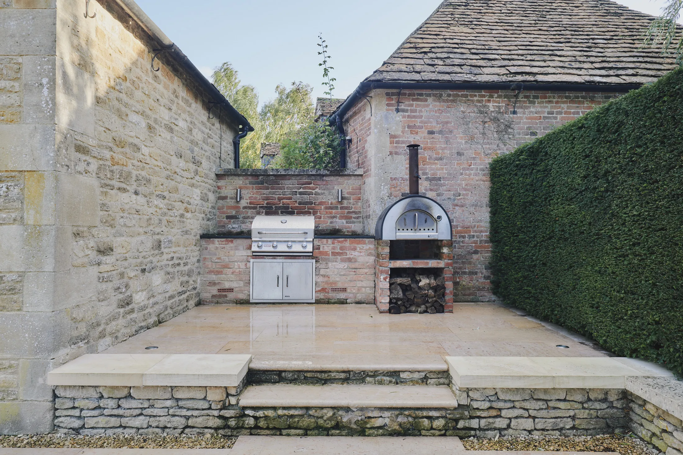 Outdoor kitchen with pizza oven and barbecue set within walled garden at Havenwood luxury short term property in The Cotswolds.