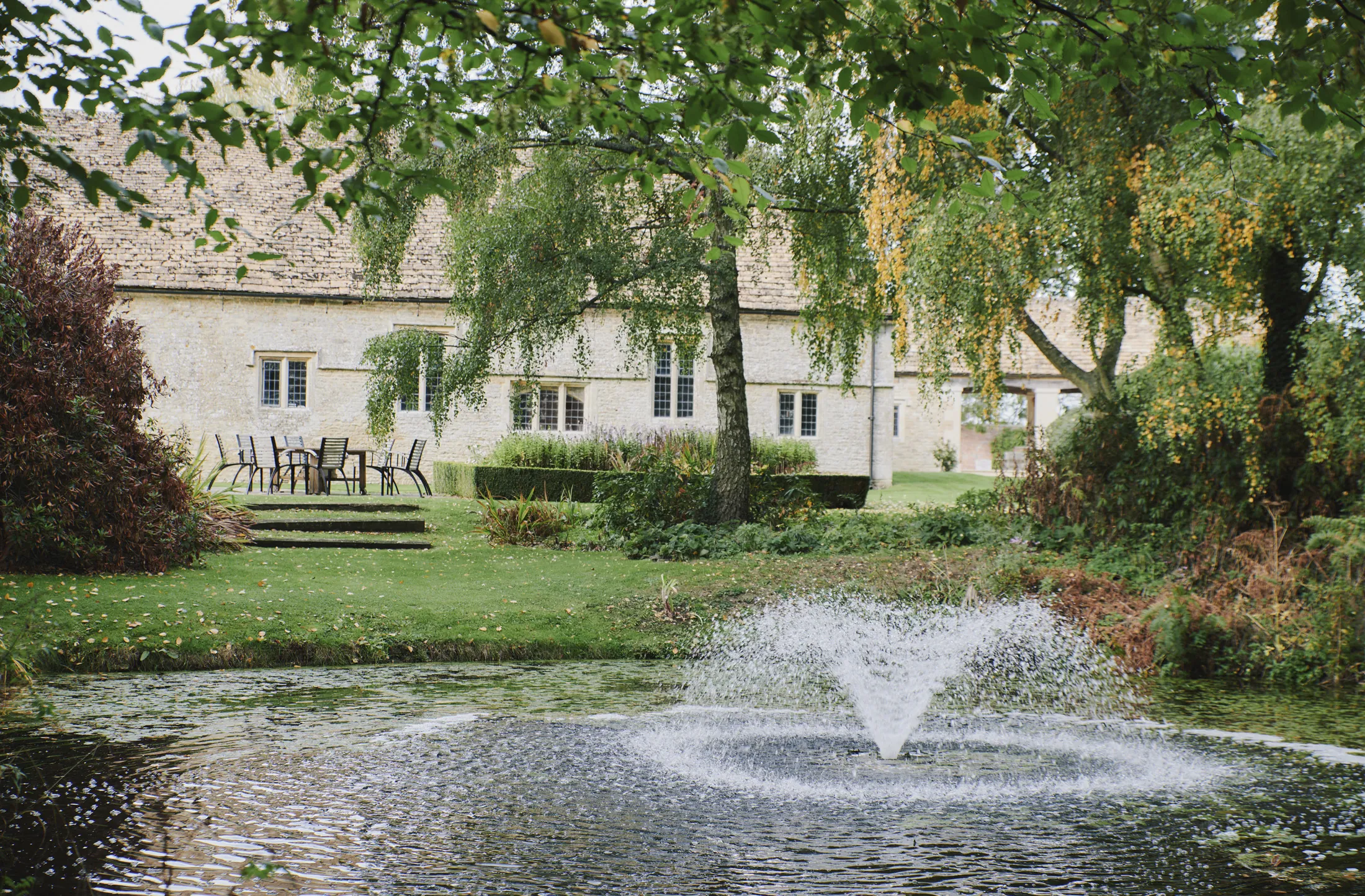 Garden pond with fountain and terrace seating at Havenwood, a Domus Stay luxury countryside property in The Cotswolds.