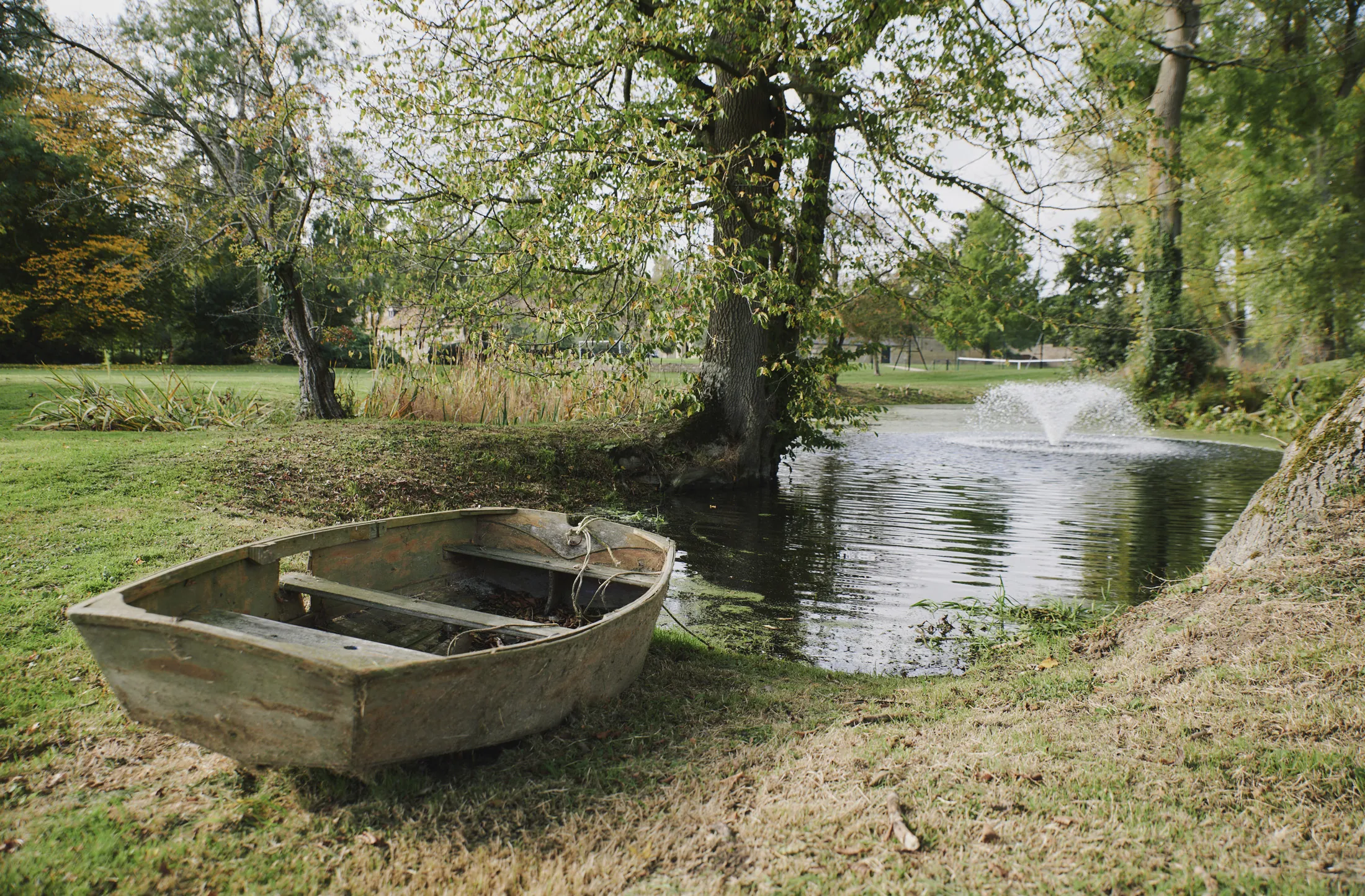 Weathered rowing boat beside tranquil pond surrounded by mature trees at Havenwood exclusive short stay rental in The Cotswolds.