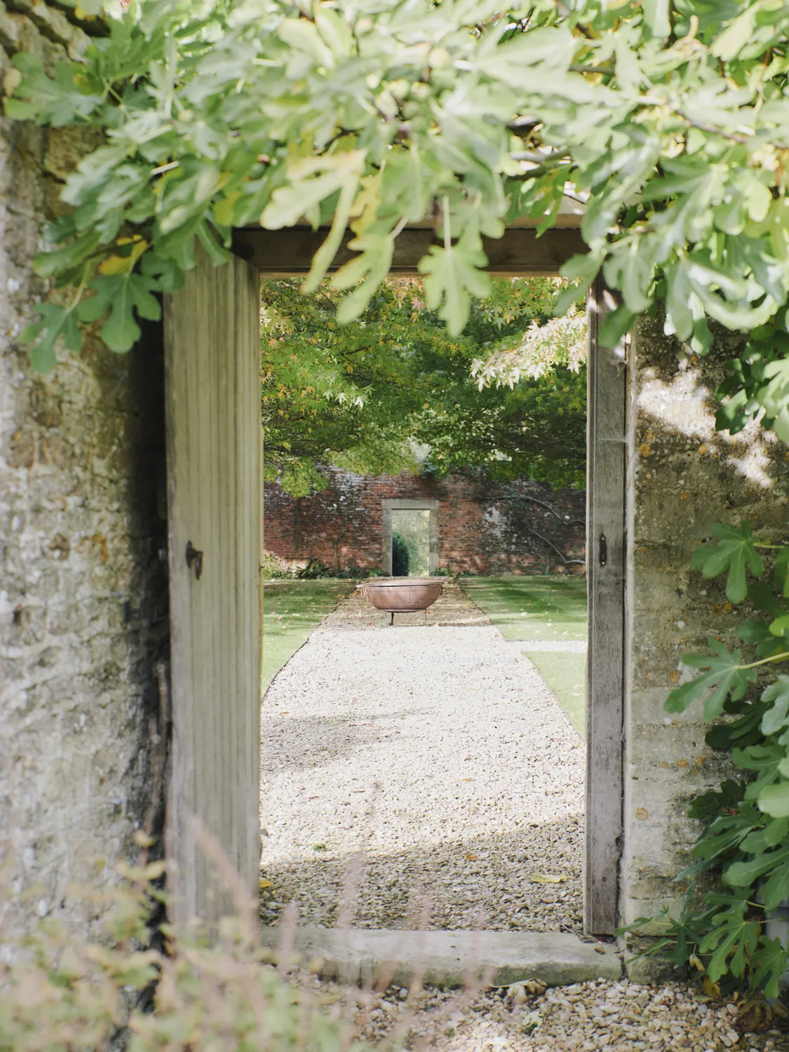 Stone archway opening onto pebbled garden path with circular water feature at Havenwood exclusive countryside retreat in The Cotswolds.