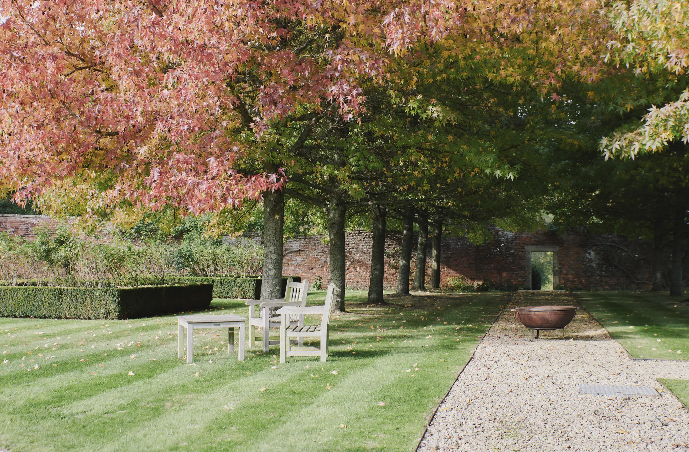 Autumn garden with wooden seating beneath golden trees and brick archway at Havenwood, a Domus Stay countryside escape.