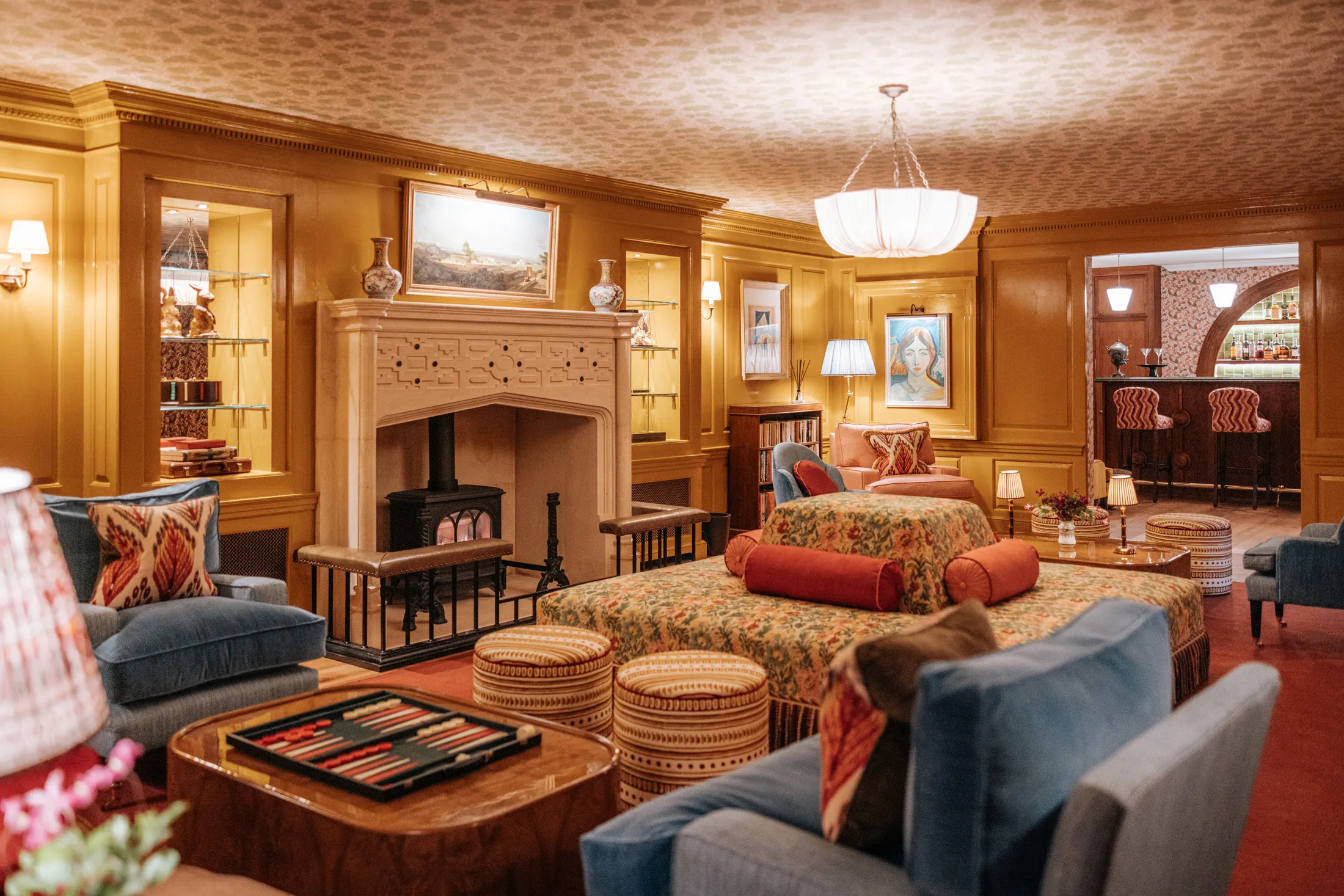 Cosy entertainment lounge at Coombe End, a Domus Stay premium holiday rental, with patterned sofas, wood panelling and a feature fireplace beside the private bar.