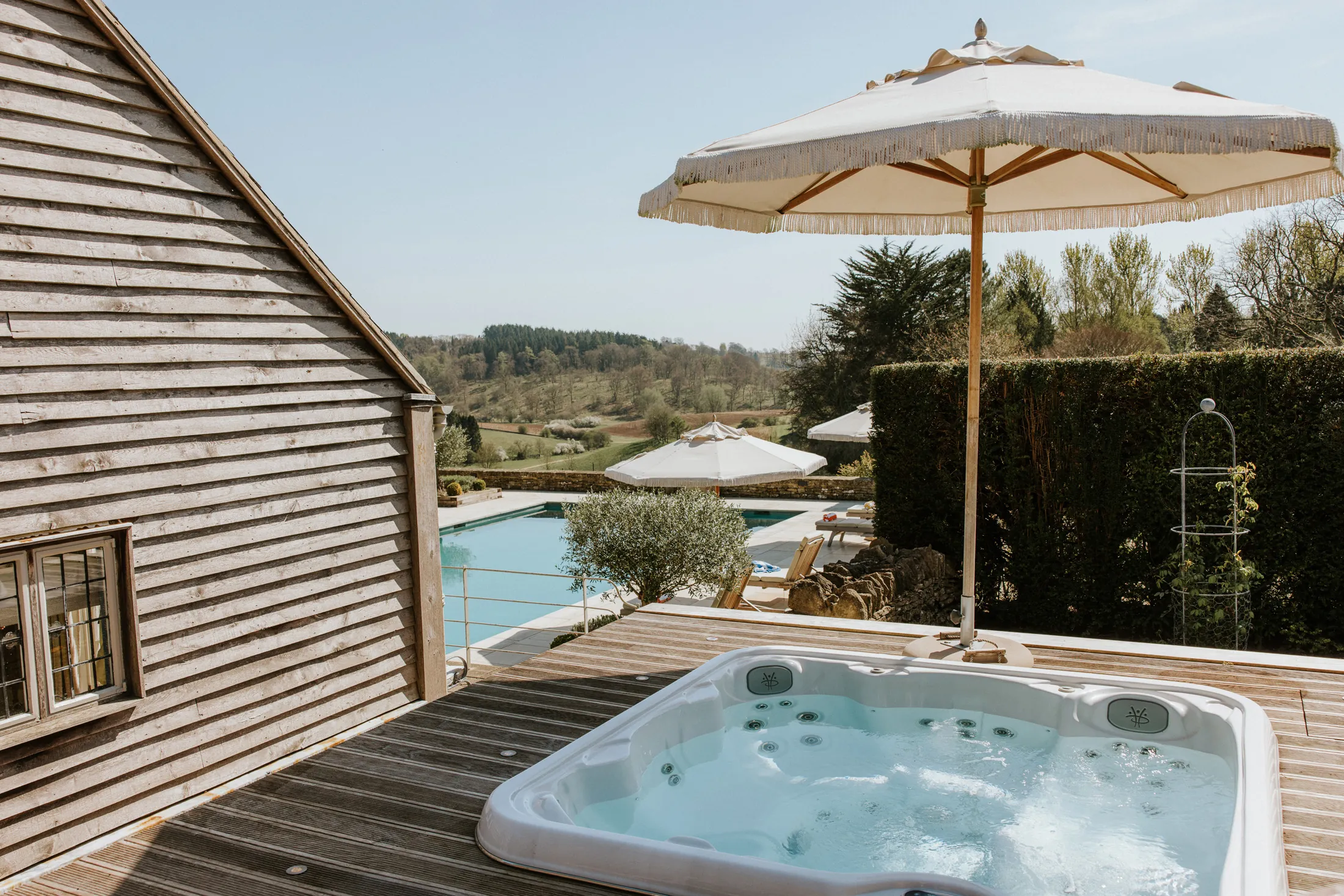 Elevated hot tub deck at Coombe End, part of the Domus Stay luxury Cotswolds collection, overlooking the outdoor pool and rolling countryside.