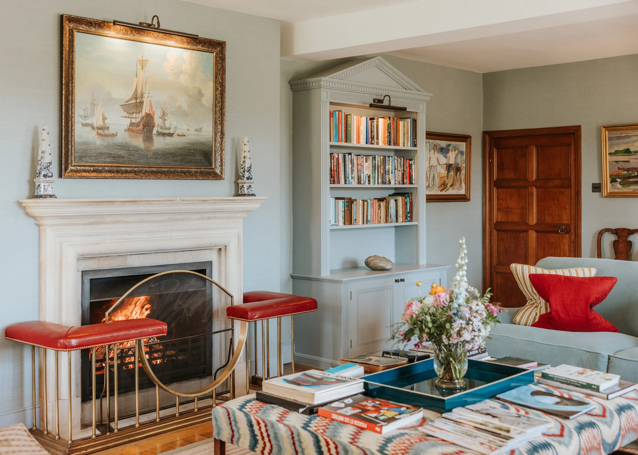 Light-filled sitting room at Coombe End, one of Domus Stay’s luxury Cotswolds retreats, with a marble fireplace, bookcase and vibrant soft furnishings.