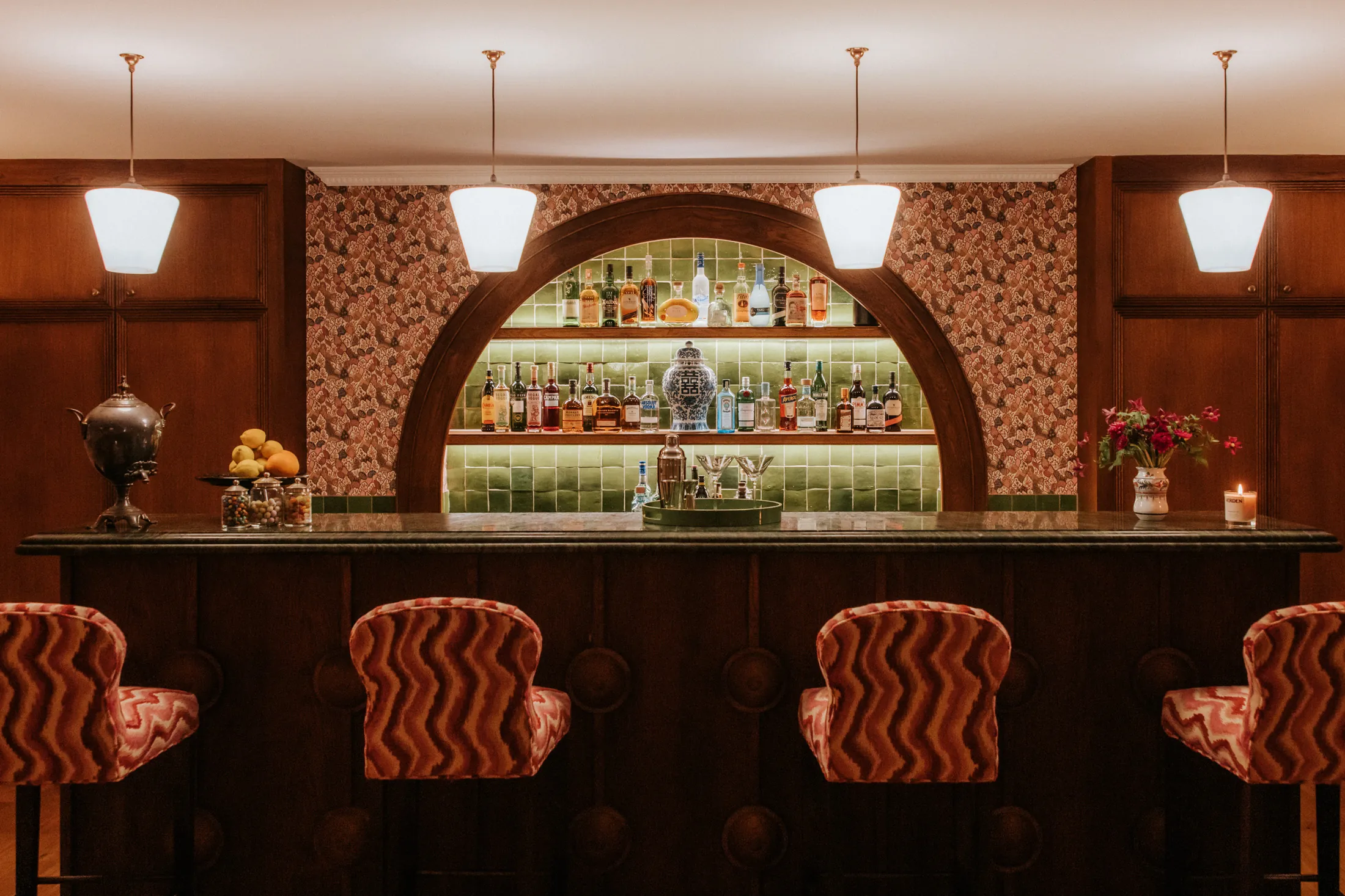 Intimate bar at Coombe End, part of the Domus Stay luxury short-stay collection, with an arched green-tiled back bar, warm lighting and patterned bar stools.