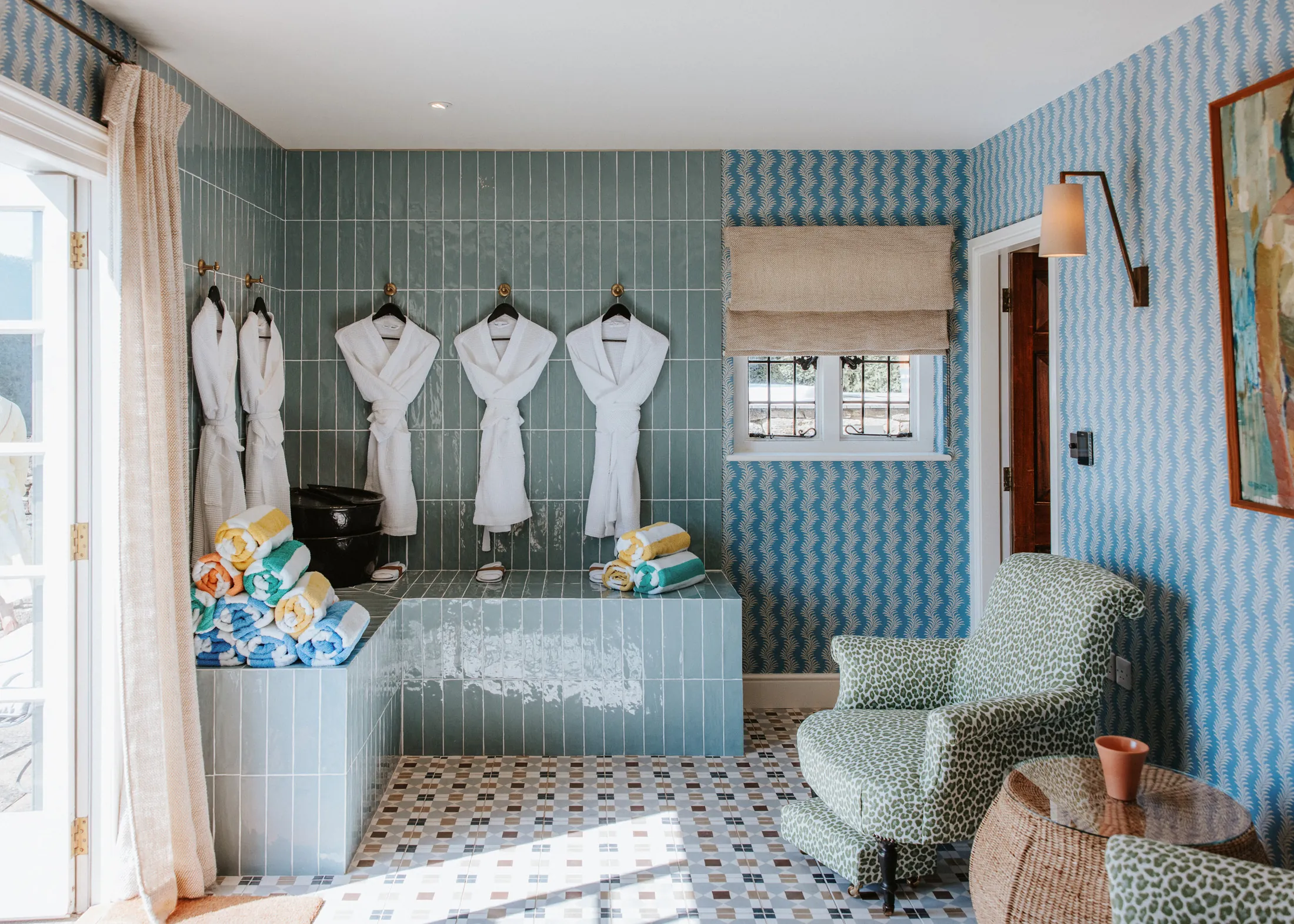 Stylish pool changing room at Coombe End, a Domus Stay premium short-stay, with tiled benches, robes, patterned walls and colourful towels.
