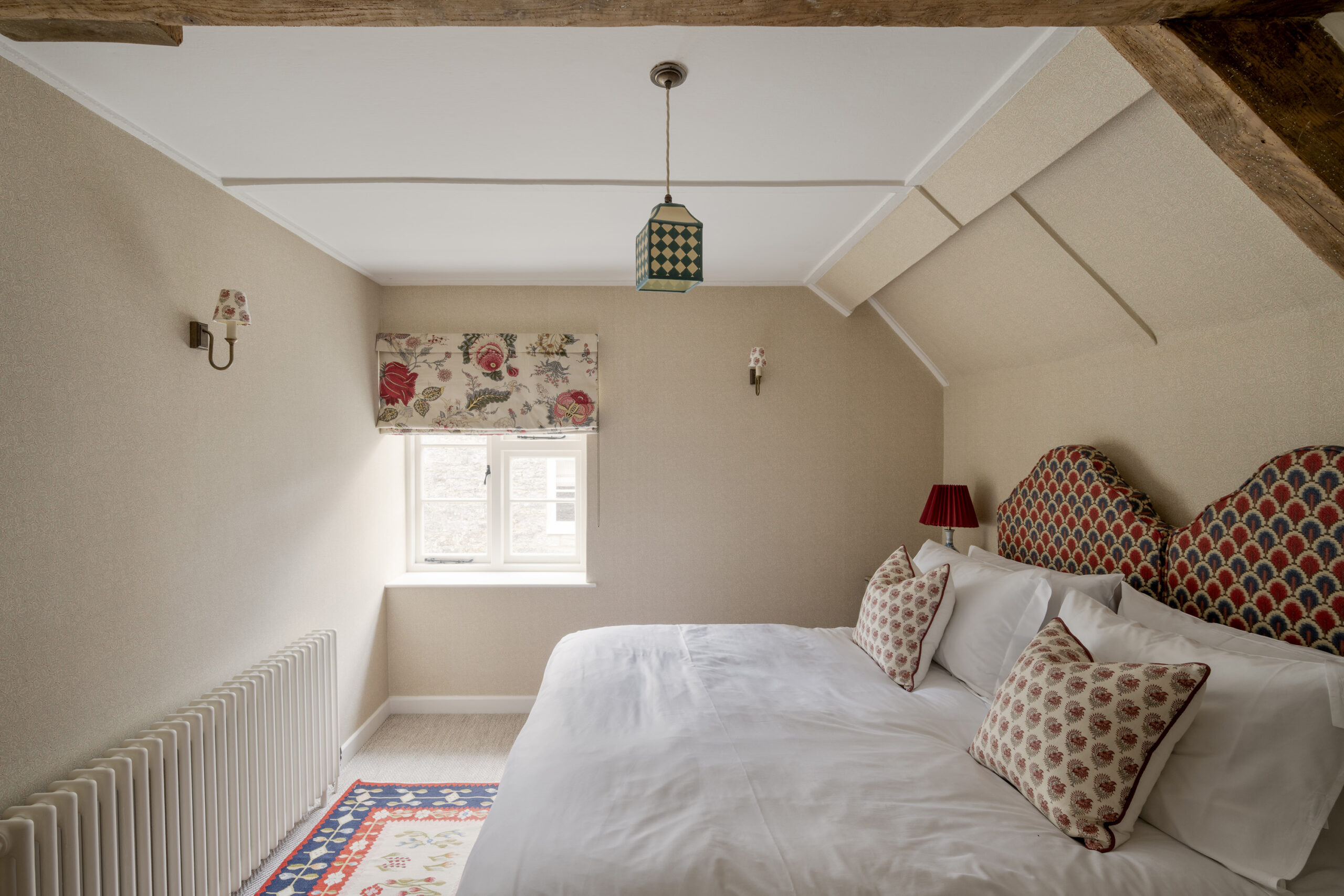Characterful bedroom with exposed beam, patterned headboards and floral accents at Ford Cottage, offered by Domus Stay as a luxury short-stay rental in The Cotswolds.