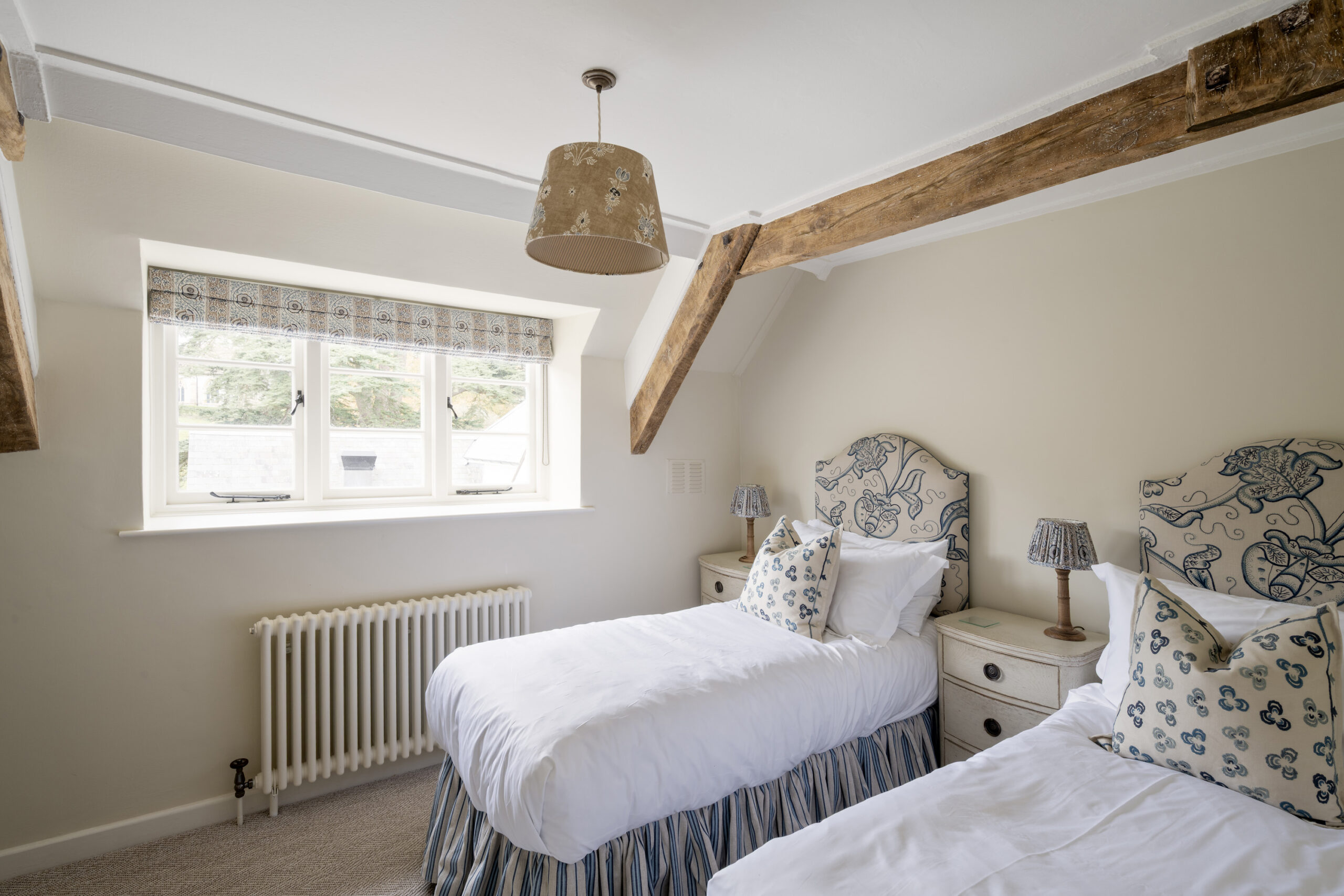 Charming twin bedroom with exposed beams, printed headboards and soft neutral tones at Ford Cottage, presented by Domus Stay as a luxury short-stay rental in The Cotswolds.
