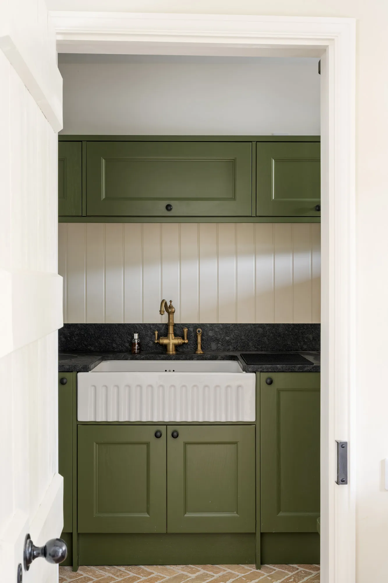 Traditional utility room at Ford Cottage, a Domus Stay luxury countryside rental in The Cotswolds, with olive cabinetry, a farmhouse sink, brass taps and panelled walls.