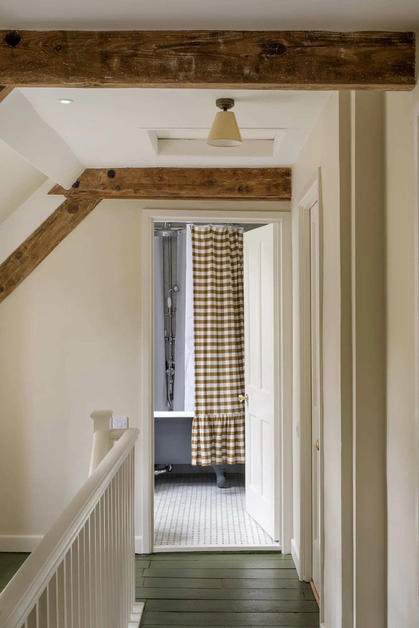 Upper landing at Winterbourne House with exposed beams, painted floorboards and a checked shower curtain beyond, part of Domus Stay’s luxury short stay collection in The Cotswolds.